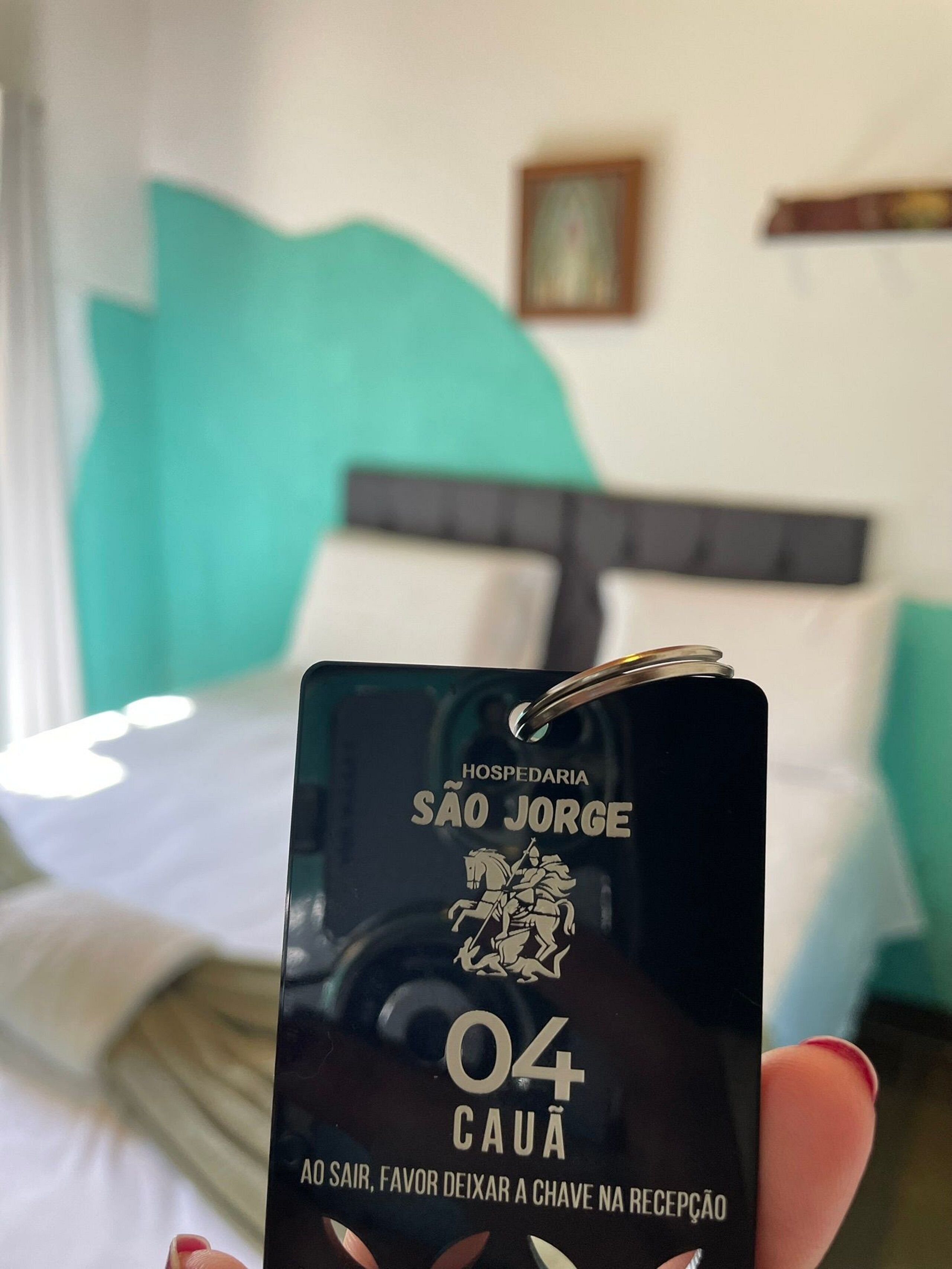 A black tag with text indicating a hotel named 'Hospedaria São Jorge' and a room number '04 Cauã'.