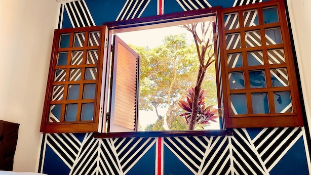 A room with a bed, a window with wooden shutters, and a wall with a geometric pattern. - Hospedaria & Galeria de Arte São Jorge  (Alto Paraíso de Goiás)