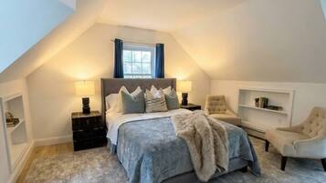 A bedroom with a bed, bedside tables, a chair, a window, and a sloped ceiling.