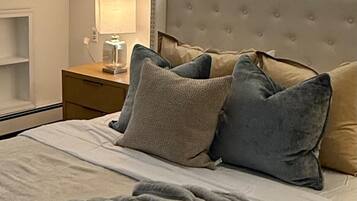A bedroom with a bed, pillows, a nightstand, a lamp, and a window.