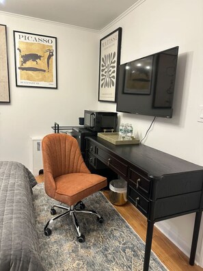 A bedroom with a bed, a desk, a chair, a TV, and two framed artworks on the wall.