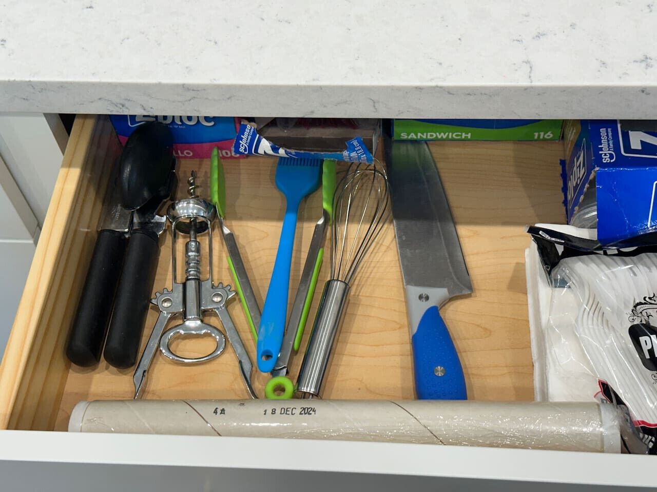 A drawer with various kitchen utensils including a corkscrew, whisk, and spatula.
