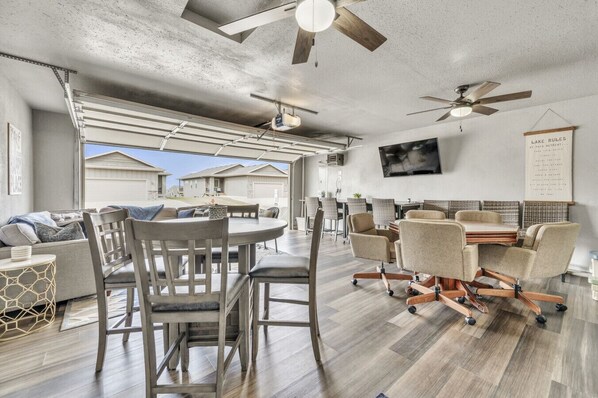 A spacious living area with a large dining table, comfortable seating, and a ceiling fan.