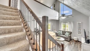 A spacious living area with a high ceiling, a staircase with wooden railings, and a view of the outdoors through large windows. - The 245 Club is located within the vacation cabin community at Bridges Bay Resort (Arnolds Park)