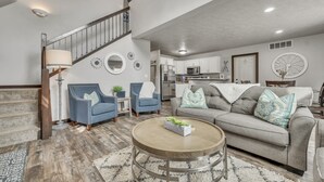 A spacious living room with a staircase, a grey sofa set, and a round coffee table. - The 245 Club is located within the vacation cabin community at Bridges Bay Resort (Arnolds Park)