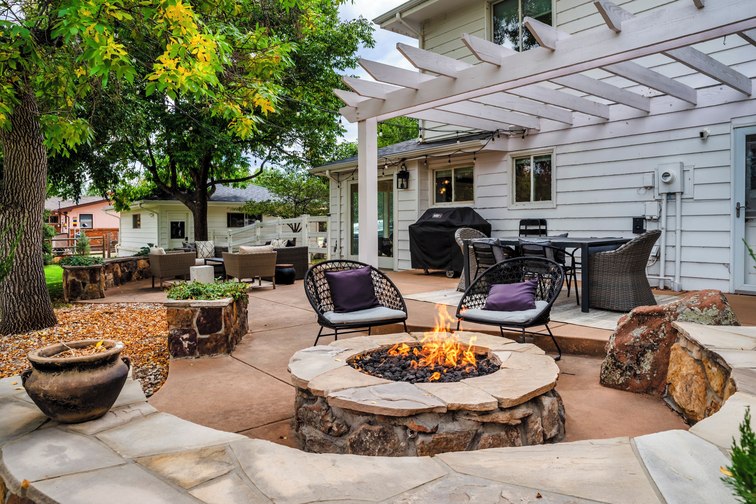 An outdoor patio with stone fire pit, wicker furniture, and a pergola.