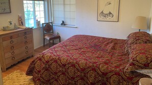 Un dormitorio con una cama grande, un aparador de madera, una silla, una ventana con persianas y un cuadro en la pared.