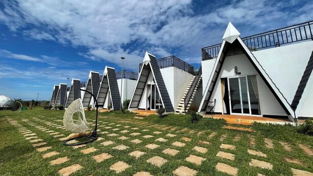 A row of modern, triangular-roofed buildings with a clear sky and a geometric sculpture in the foreground. - Romnea Moon Resort (Krong Saen Monourom)