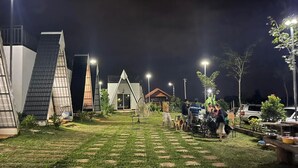 A courtyard with a modern building, a small house, and a dining area with people. - Romnea Moon Resort (Krong Saen Monourom)