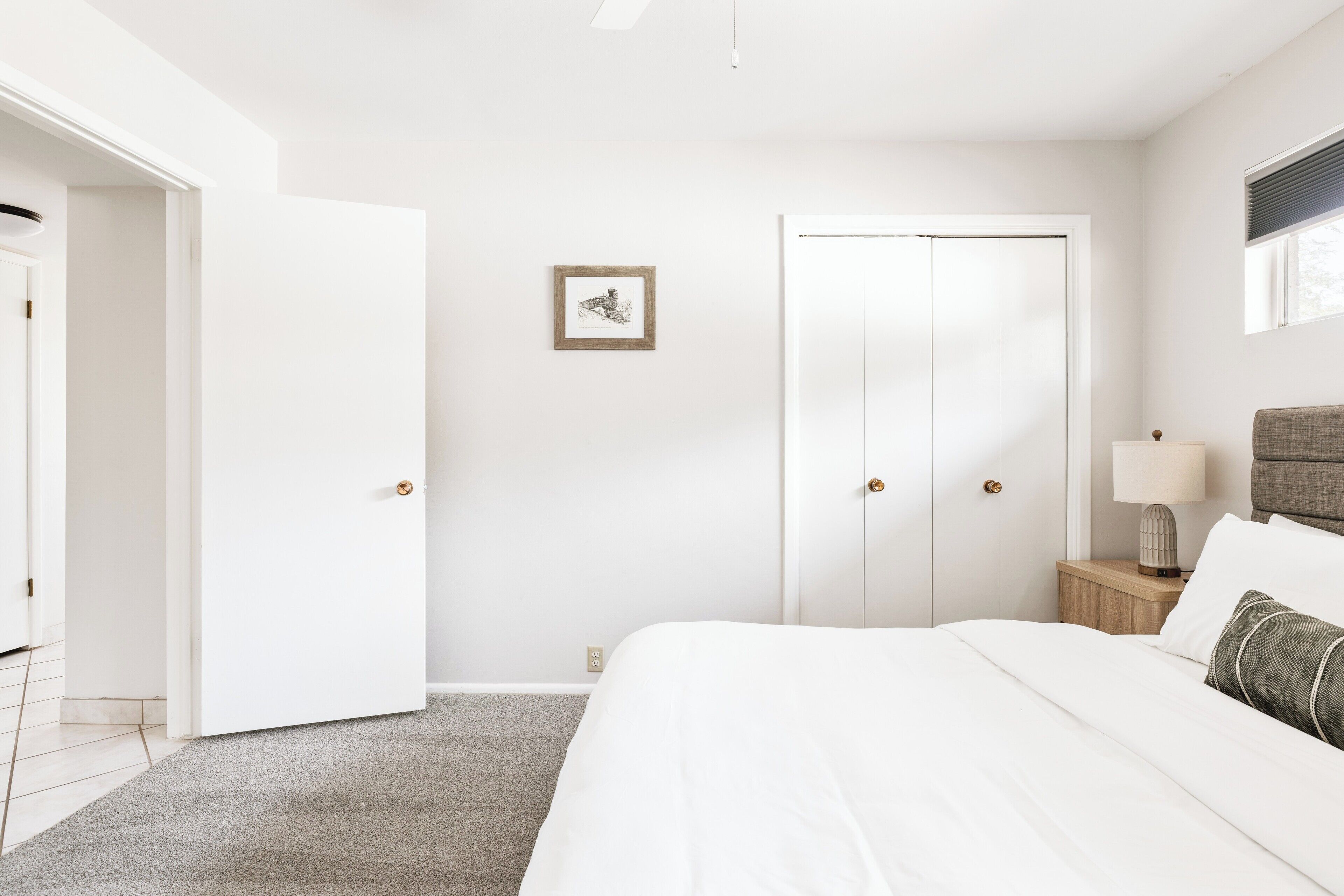 Una camera da letto con un letto, un comodino con una lampada, un quadro appeso al muro e un armadio.