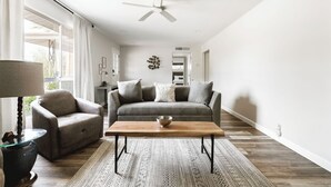 A modern living room with a sofa, armchair, and coffee table, a ceiling fan, and a patterned rug.