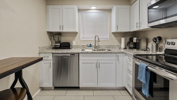 Una cocina compacta con gabinetes blancos, lavavajillas, estufa y microondas.