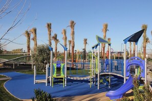 Un parque infantil con estructuras para escalar, toboganes y superficie de goma azul.