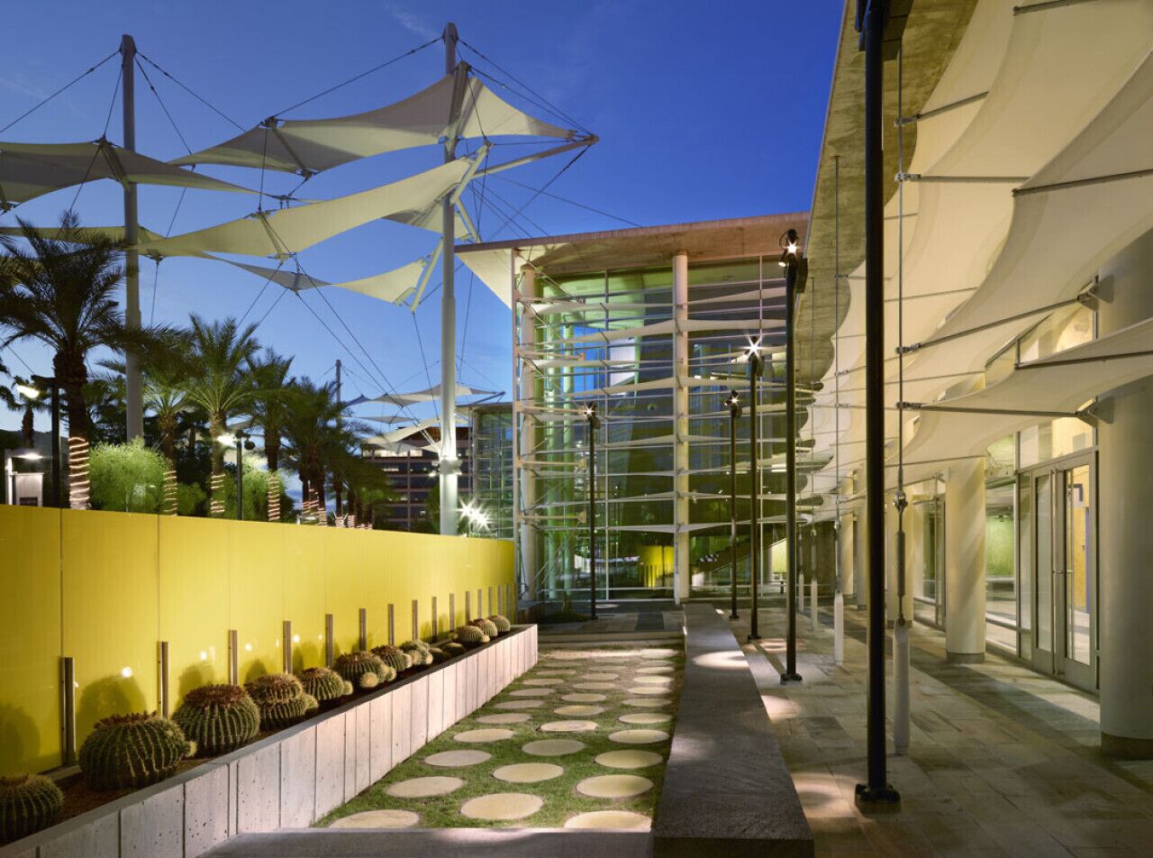 A modern building with a glass facade, a yellow wall with cactus planters, and a covered walkway.