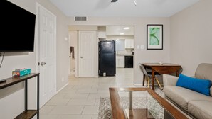 A living room with a TV, a sofa, a coffee table, and a ceiling fan. - Clean Quiet Condo - Reliable AC - Downtown Mesa - Free Parking (Mesa)