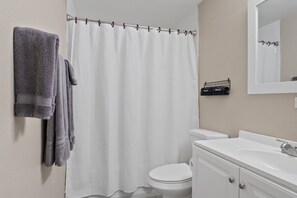 A bathroom with a white shower curtain, a white toilet, a white sink with a mirror, and a towel rack with towels. - Clean Quiet Condo - Reliable AC - Downtown Mesa - Free Parking (Mesa)