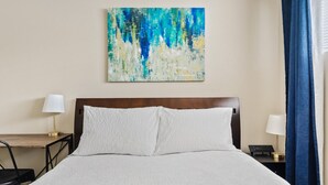 A hotel room with a bed, two bedside tables, a desk, and a painting on the wall. - Clean Quiet Condo - Reliable AC - Downtown Mesa - Free Parking (Mesa)