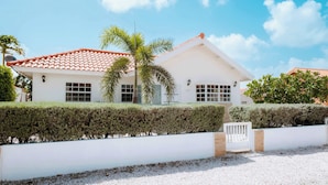 A white building with a red-tiled roof, a white gate, and a gravel driveway. - Casa del Sol (Noord)