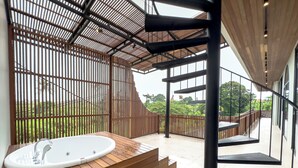 Ein modernes Badezimmer mit freistehender Badewanne, Holzboden und Blick auf üppiges Grün.