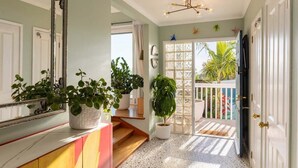 Un pasillo con una escalera, plantas en macetas, un espejo grande y vistas al exterior.