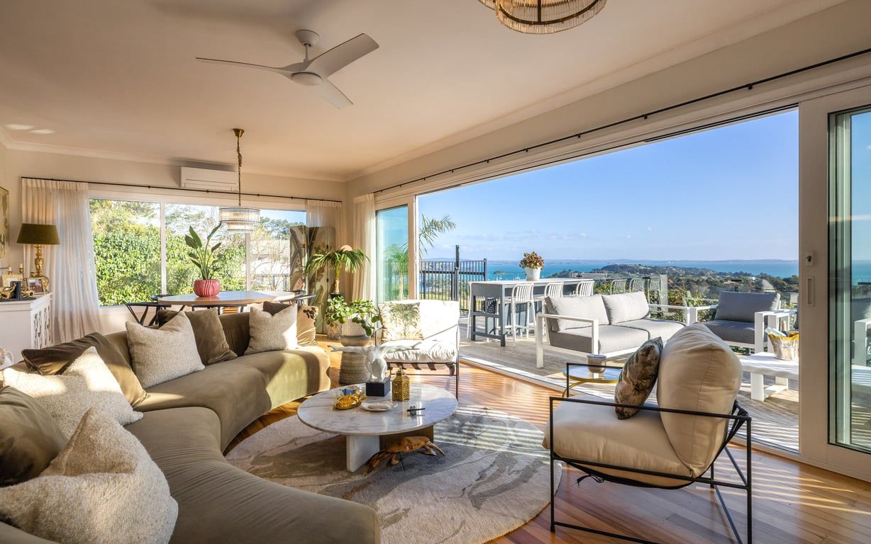 A spacious living area with a large sofa, a coffee table, and a view of the ocean through large windows.
