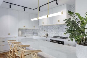 A modern kitchen with white cabinetry, a marble island, and a potted plant.