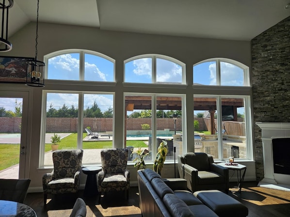 A spacious living room with large windows, a fireplace, and outdoor patio furniture. - Family Fun Oasis (FATE)