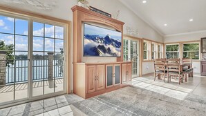 A spacious living room with a large TV, sliding glass doors to a balcony, and a dining area. - Morehead Retreat on 75 ft of East Lake Okoboji (Spirit Lake)
