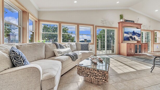 A spacious living room with a beige sectional sofa, a glass coffee table, and a stone fireplace. Large windows offer views of the outdoors. - Morehead Retreat on 75 ft of East Lake Okoboji (Spirit Lake)