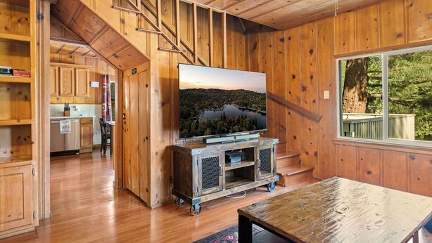 A wooden interior with a TV on a cart, a staircase, and a view of a forest through a window.