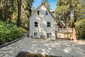 Une maison à deux étages avec un mur de soutènement en pierre, une terrasse et un escalier menant à un deuxième niveau.