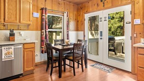 A cabin-style kitchen with wooden cabinets, a dining table with chairs, a built-in oven, and a sliding glass door leading to an outdoor patio.