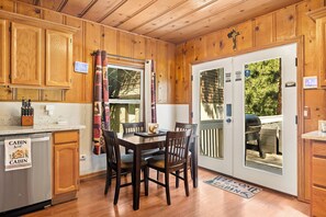 A cabin-style kitchen with wooden cabinets, a dining table with chairs, a built-in oven, and a sliding glass door leading to an outdoor patio.