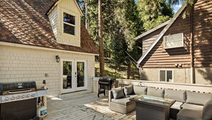 A wooden deck with a grill, outdoor furniture, and a view of a cabin.