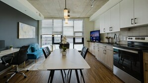 Een moderne keuken met witte kasten, een zwarte kookplaat en een eethoek met een tafel en stoelen.