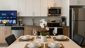 Een moderne keuken met witte kasten, roestvrijstalen apparatuur en een eethoek voor zes personen met zwarte stoelen en een witte centrale tafel.