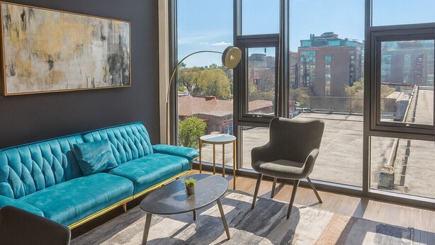 Een moderne woonkamer met een blauwe bank, een salontafel en een stoel. Er is een groot raam met uitzicht op de stad.