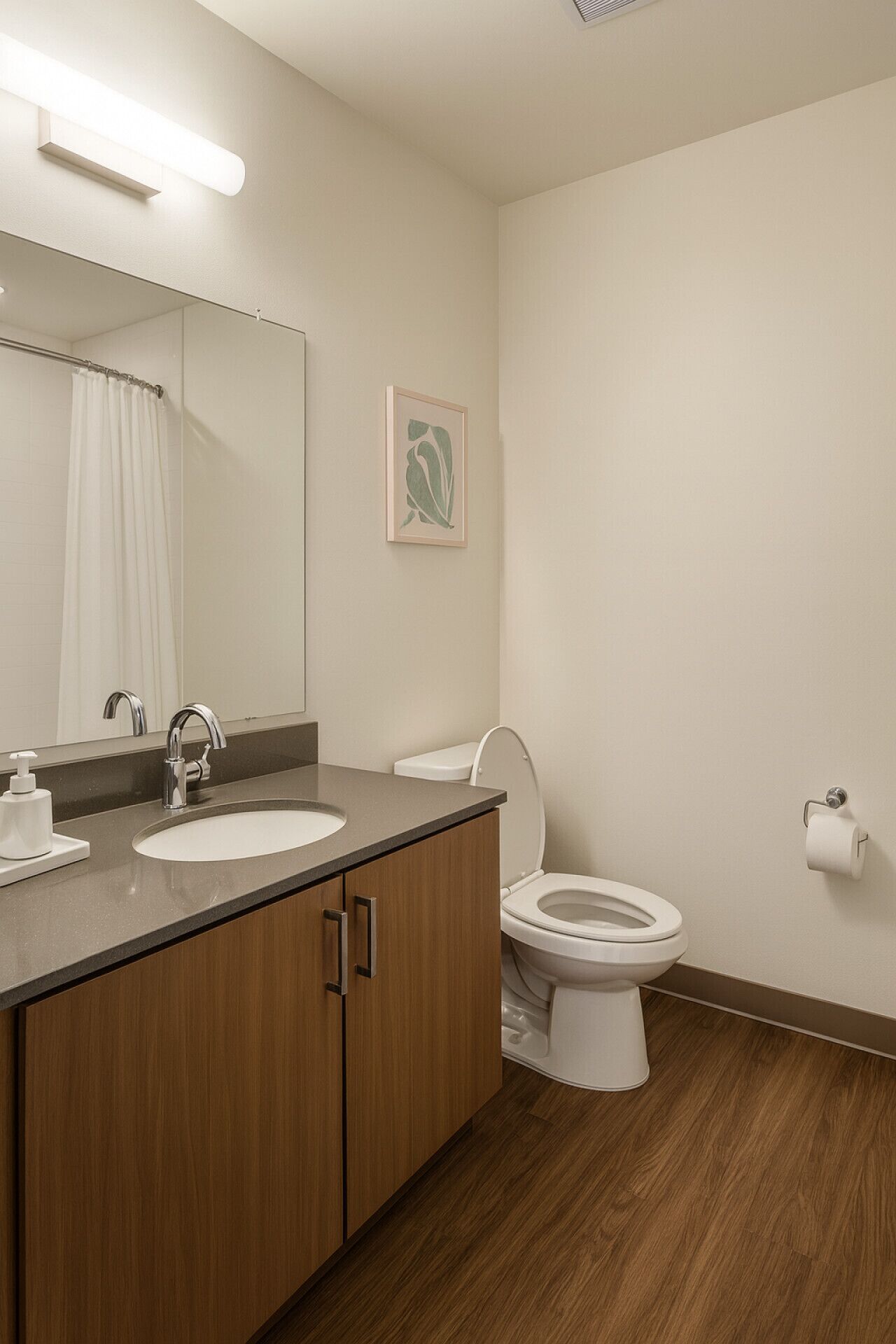 A modern bathroom with a wooden vanity, a sink, a mirror, a toilet, and a framed artwork on the wall.