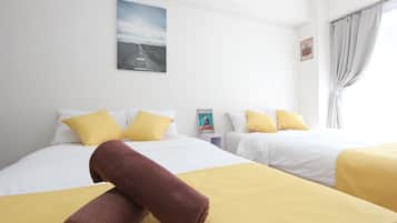 A hotel room with two beds, each with white bedding and yellow pillows. There is a rolled brown towel on the bed in the foreground.
