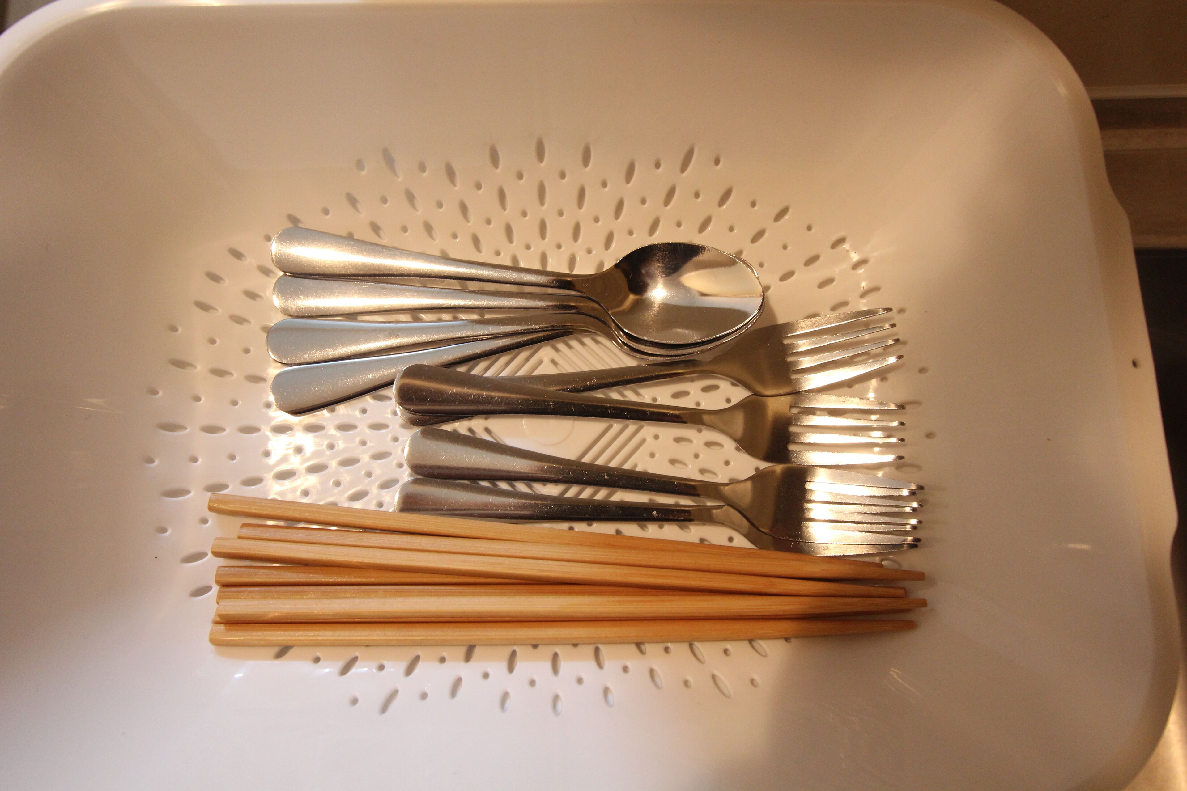 A white colander with various utensils, including spoons, forks, and chopsticks, arranged on it.