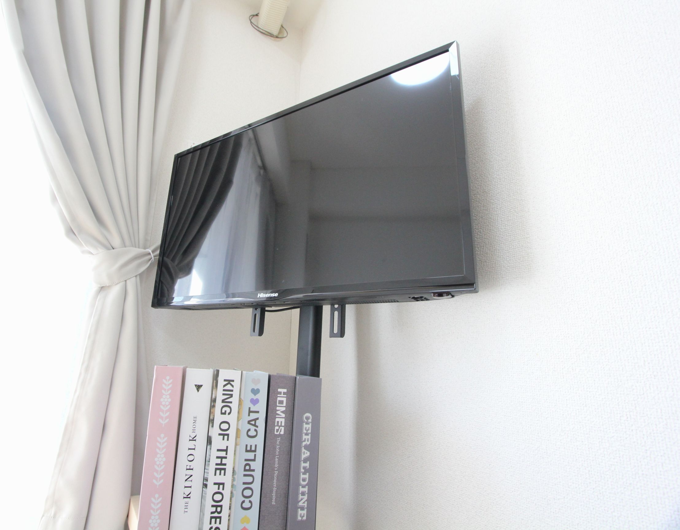 A flat-screen TV mounted on a wall with a curtain partially covering it.