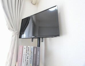 A flat-screen TV mounted on a wall with a curtain partially covering it. - Shinjuku 1-Stop! Walk to Hatsudai / 4-Person Stay with Wi-Fi (B) (渋谷区本町)