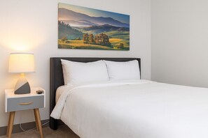 A neatly made bed with white linens, a dark headboard, and a bedside table with a lamp.