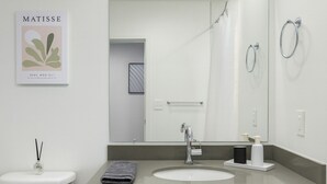 Een moderne badkamer met een wit toilet, een houten wastafelmeubel met een wastafel, een grote spiegel en een douchehoek.