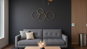 Een moderne woonkamer met een grijze bank, een houten salontafel en een rond hanglampje aan de muur.