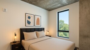 Een moderne slaapkamer met een groot bed, twee nachtkastjes met lampen, een raam met uitzicht op bomen en abstracte kunst aan de muur.