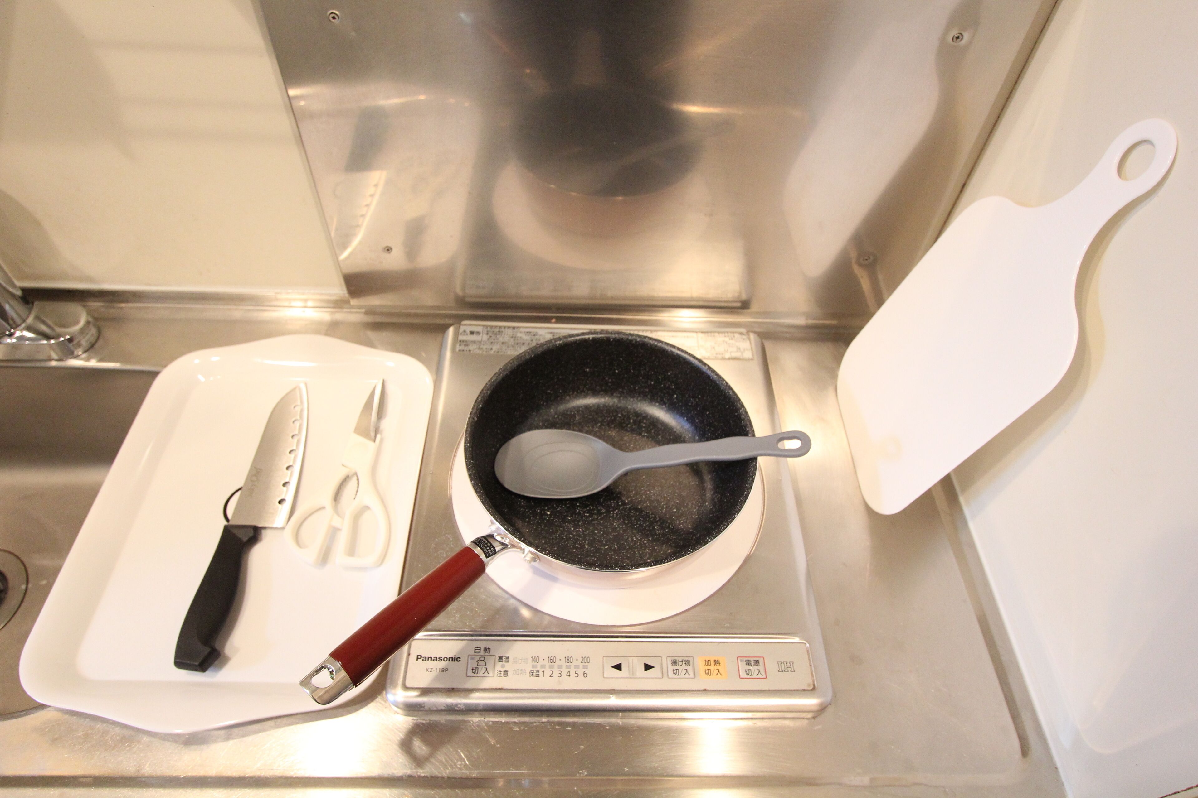 Une cuisine avec une cuisinière, une poêle, une spatule et une paire de ciseaux, le tout posé sur un plateau blanc.