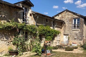 A stone building with a window, a door, and a small garden area with potted plants.