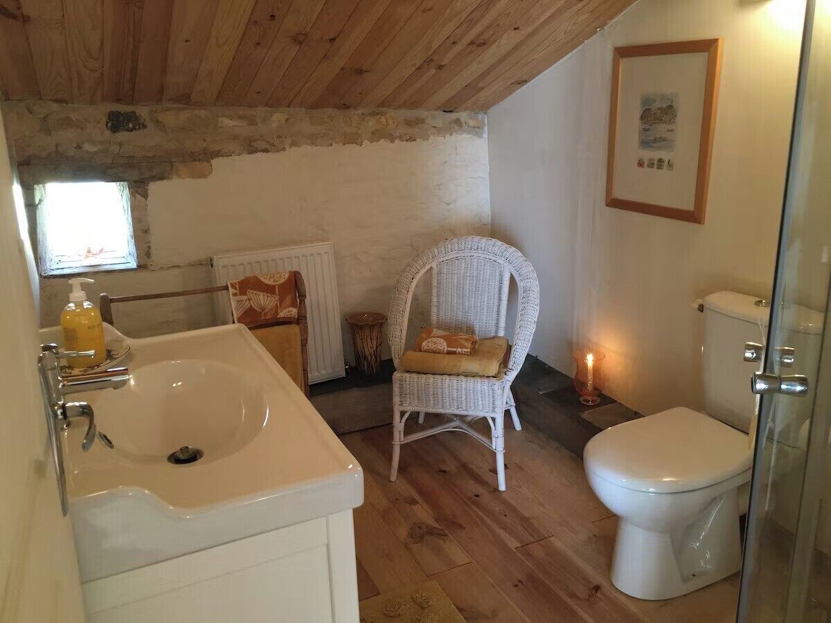 A bathroom with a white sink, a wicker chair, a toilet, and a framed picture on the wall.