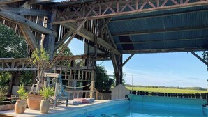 A rustic outdoor pool area with a wooden deck, a covered seating area, and a view of a green field in the background. - 3Bedrooms-Sleeps6-WiFi-Fireplace (Ceaux-en-Loudun)